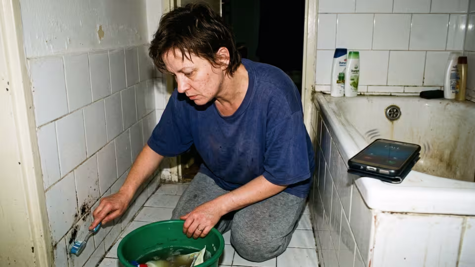 45letá žena klečí na studené dlážděné podlaze s mírně shrbenými zády a metodicky drhne zubním kartáčkem.